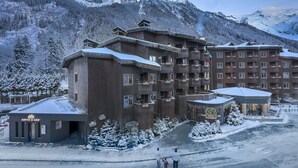 Un hotel de varios pisos con fachada de madera tradicional, balcones y un paisaje nevado con montañas al fondo.