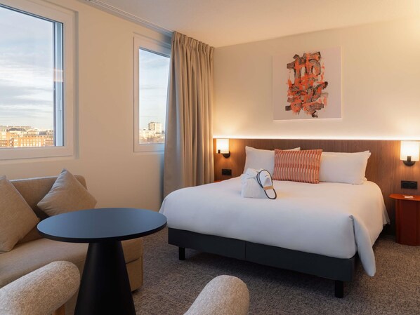 A hotel room with a bed, a round table, a sofa, and a city view.