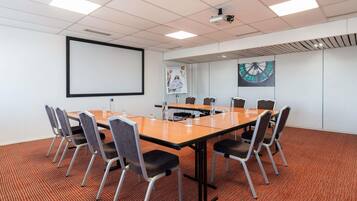 Un salón de conferencias con una gran mesa, sillas, una pantalla de proyector y un reloj en la pared.