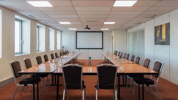 A conference room with a long table, chairs, a projector screen, and windows.