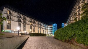 Une vue nocturne d’un immeuble à plusieurs étages, d’un chemin pavé et d’une haie bien entretenue.