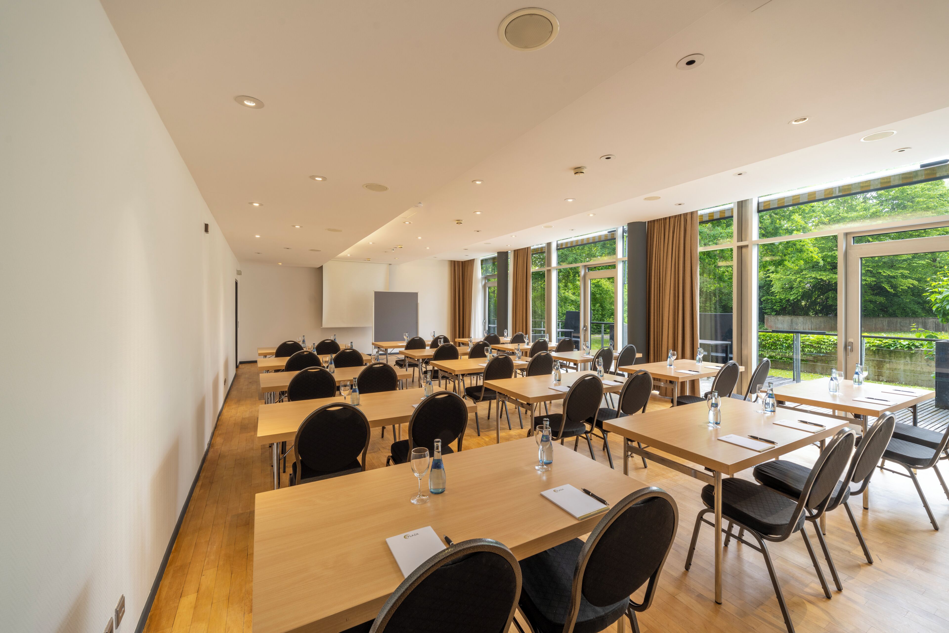 A conference room with multiple tables and chairs, large windows with curtains, and a projector screen on the wall.
