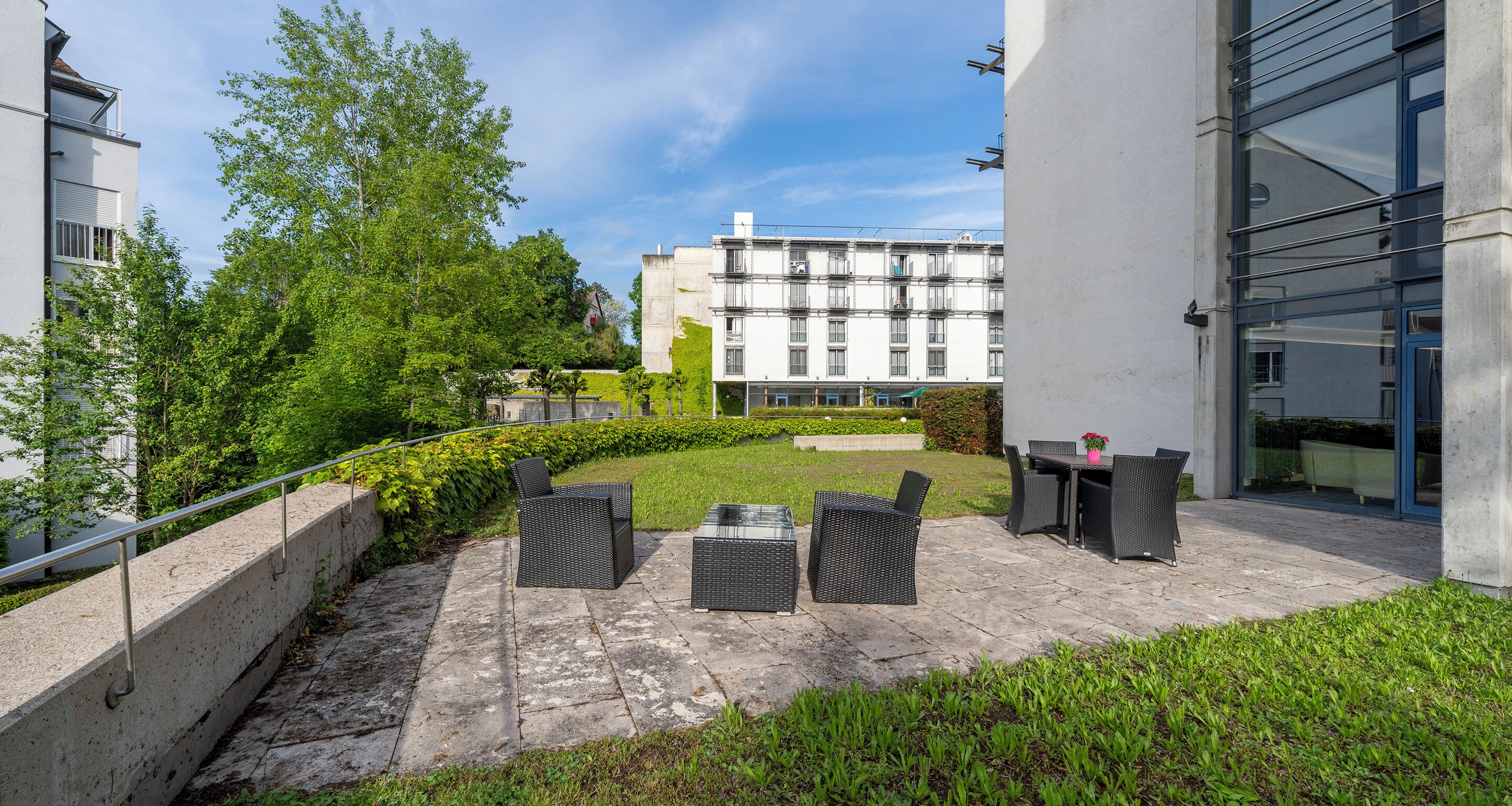 A courtyard with outdoor seating, a hedge, and a building in the background.