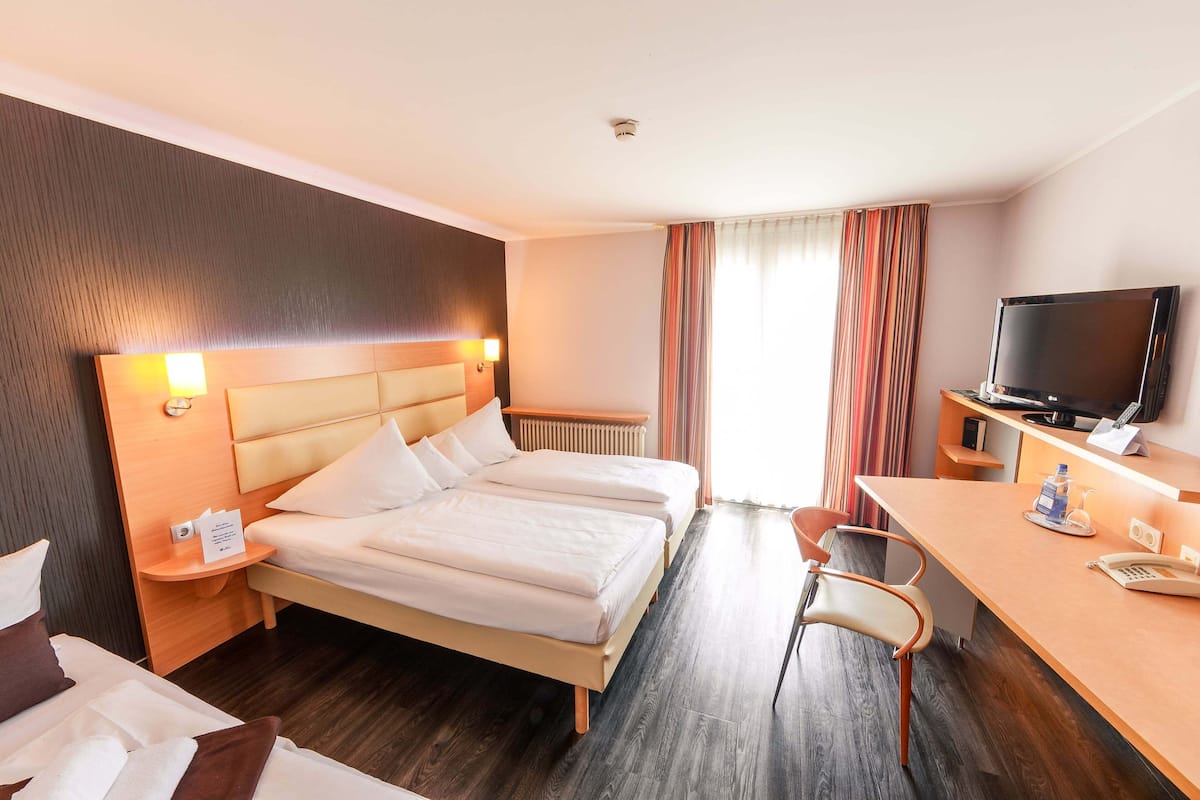 A hotel room with two beds, a desk, a chair, a television, and a window with curtains.