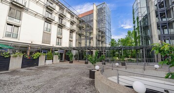 Un patio con suelo de adoquines, una zona de estar con techo de cristal y un edificio de varios pisos con balcones.