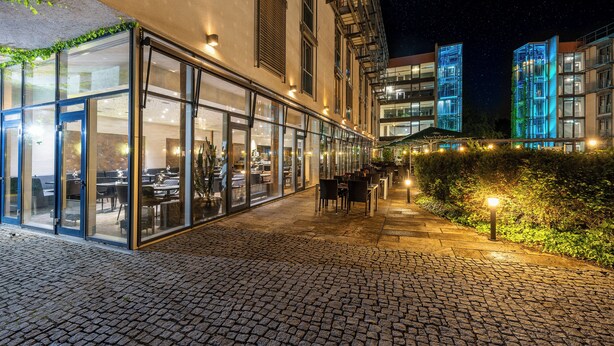 Un espace de restauration en plein air doté de murs en verre, d’un chemin pavé et d’un bâtiment bien éclairé, caractérisé par une architecture moderne.