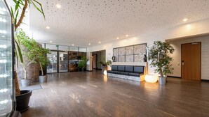 Un hall d’entrée spacieux avec un comptoir de réception, un espace salon et des plantes en pot.