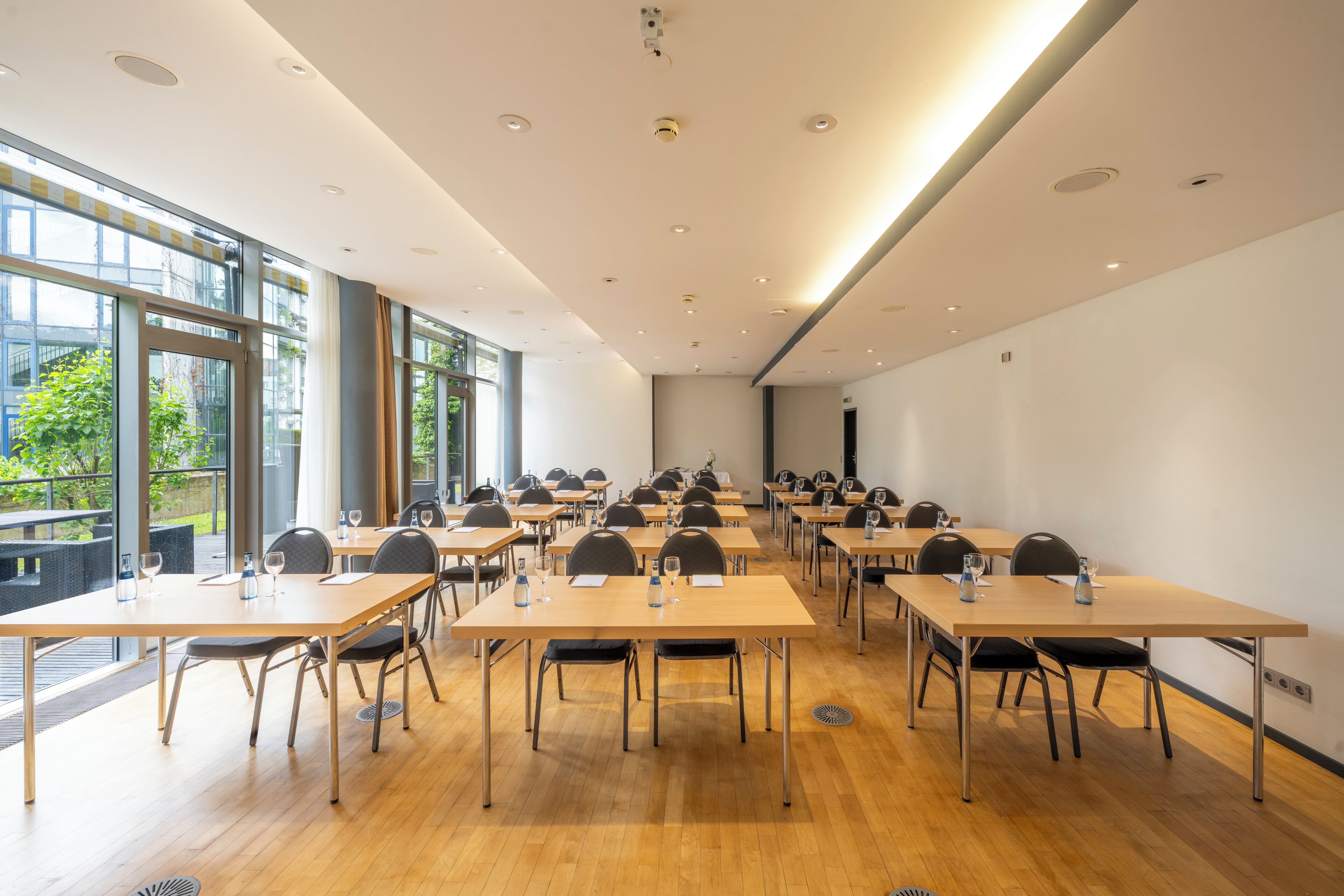 A conference room with multiple tables, chairs, and a large window providing a view of the outdoors.