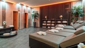Un espace de spa moderne comprenant trois tables de massage, un espace d’accueil et une étagère murale où sont rangées les serviettes.