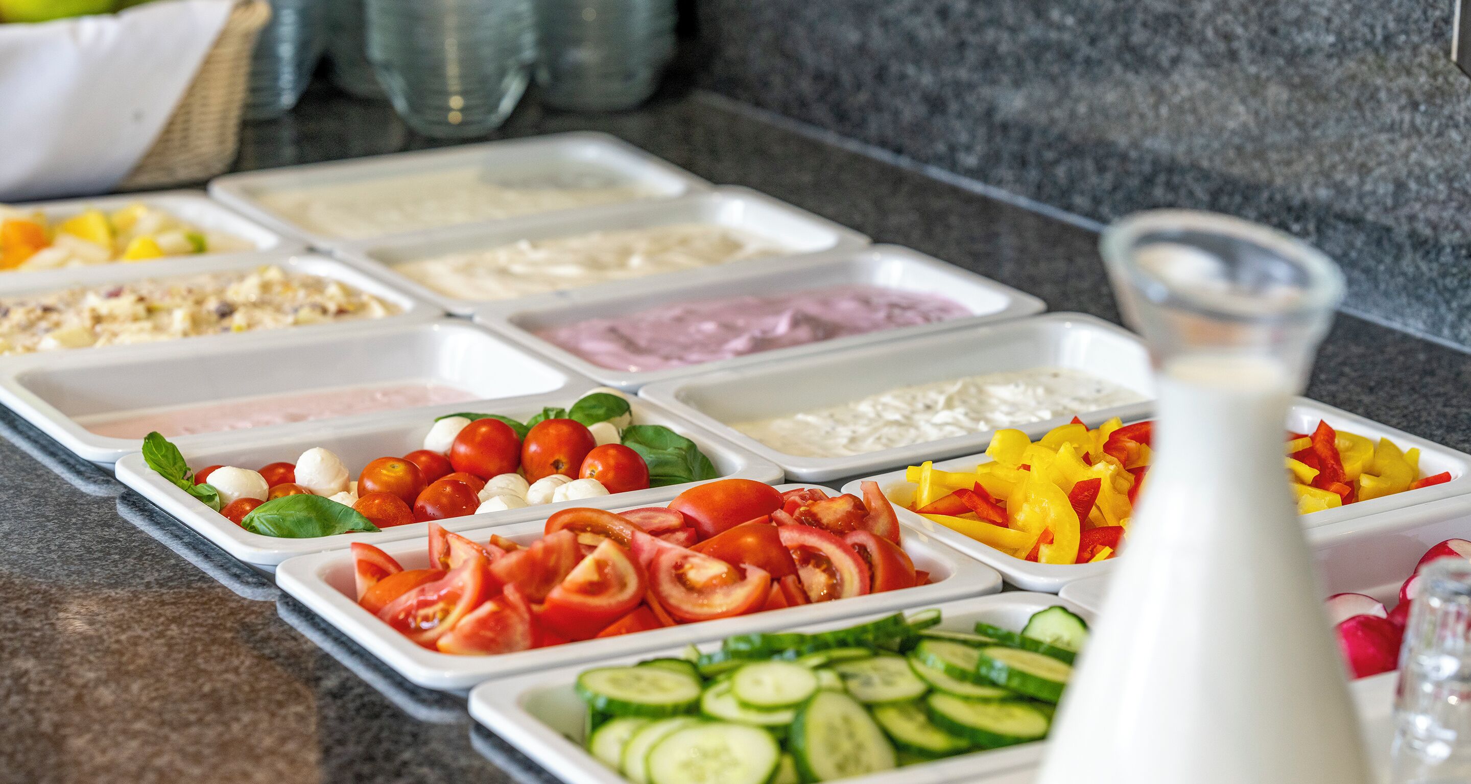 Un buffet proposant une variété de plats, notamment des tomates, des concombres, de la mozzarella et d’autres légumes.