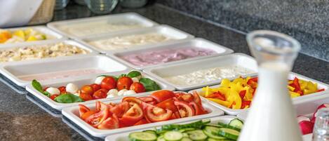 Un buffet proposant une variété de plats, notamment des tomates, des concombres, de la mozzarella et d’autres légumes.