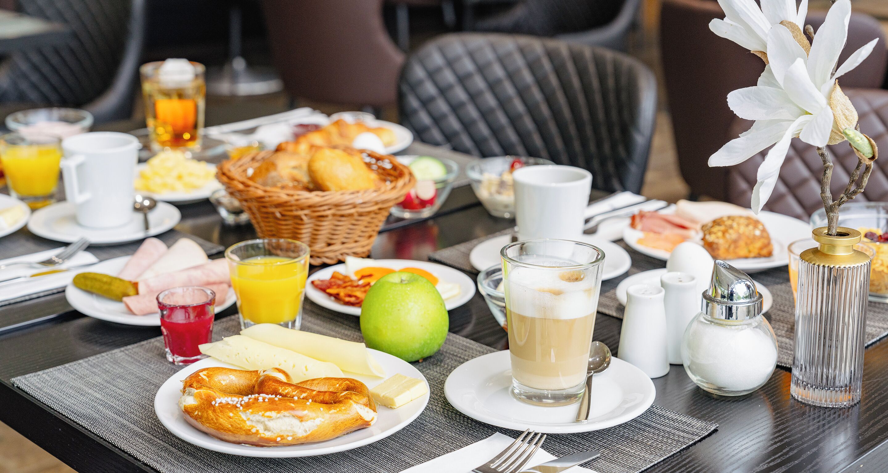 A breakfast table with various food items, a glass of juice, and a candle.