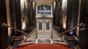 A grand staircase with marble walls and a red carpet leading to a double door. - acom Hotel Berlin Kurfürstendamm (Berlin)