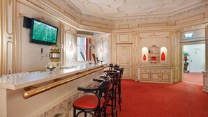 A bar area with a long counter, multiple bar stools, and a television screen displaying a sports game. - acom Hotel Berlin Kurfürstendamm (Berlin)