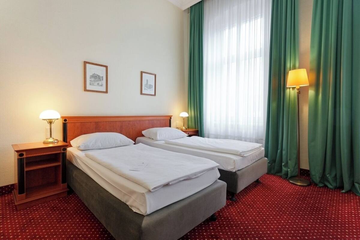 Habitación de hotel con dos camas, cabecero de madera, alfombra roja y cortina verde.
