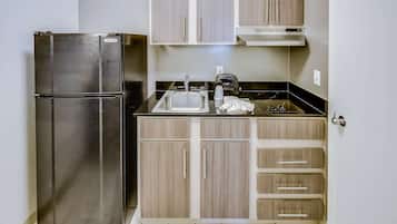Una cocina compacta con un refrigerador de acero inoxidable, un lavamanos y gabinetes de madera.