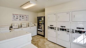 A laundry facility with multiple washing machines and dryers, a tiled floor, and instructional posters on the wall.