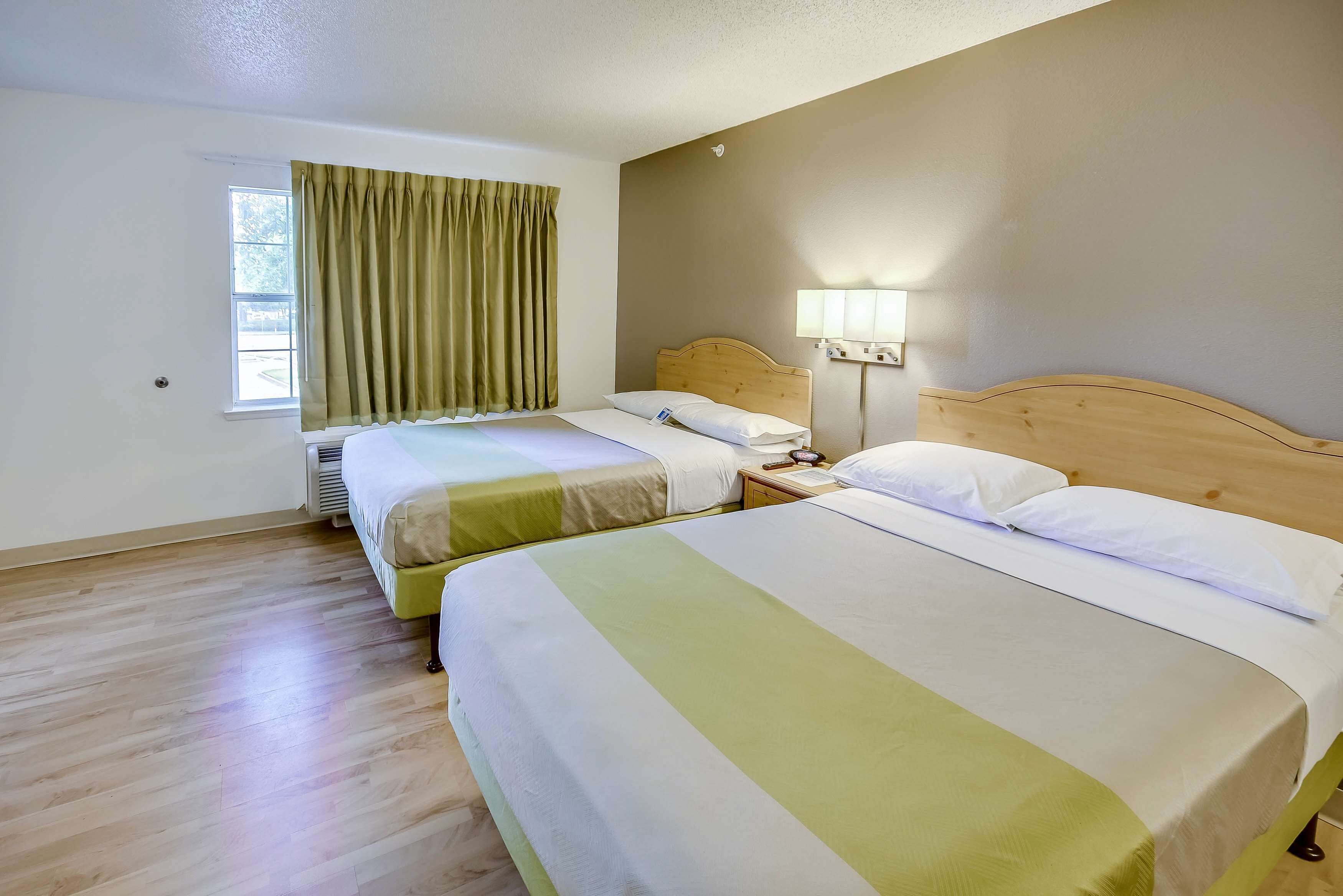 Habitación de hotel con dos camas, una ventana con cortinas, una lámpara de noche y cabecera de madera.