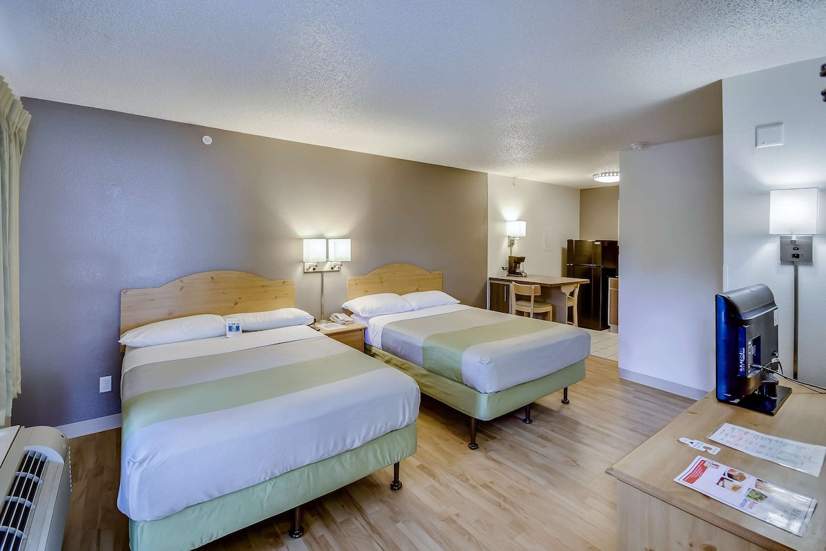 A hotel room with two beds, a desk, a coffee machine, and a TV.