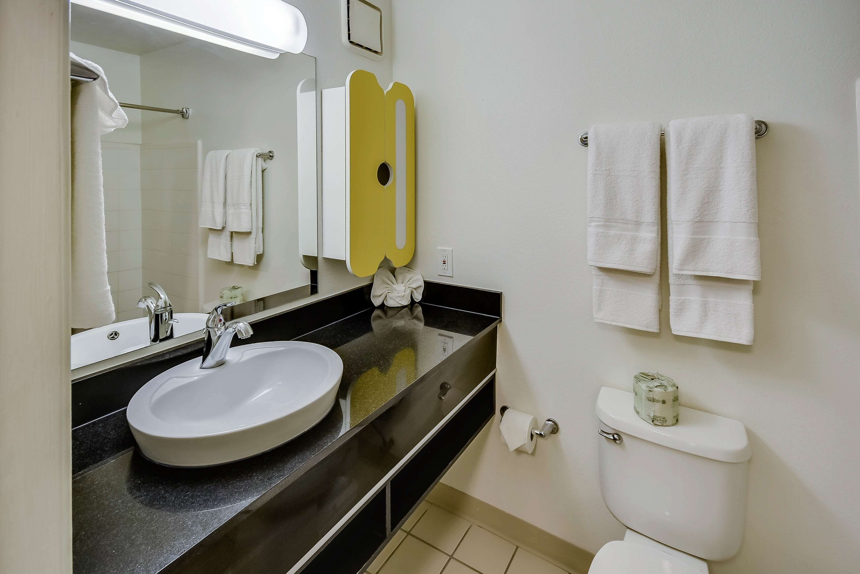 Un baño con un lavamanos blanco, un espejo, un inodoro y dos toallas colgadas en la pared.