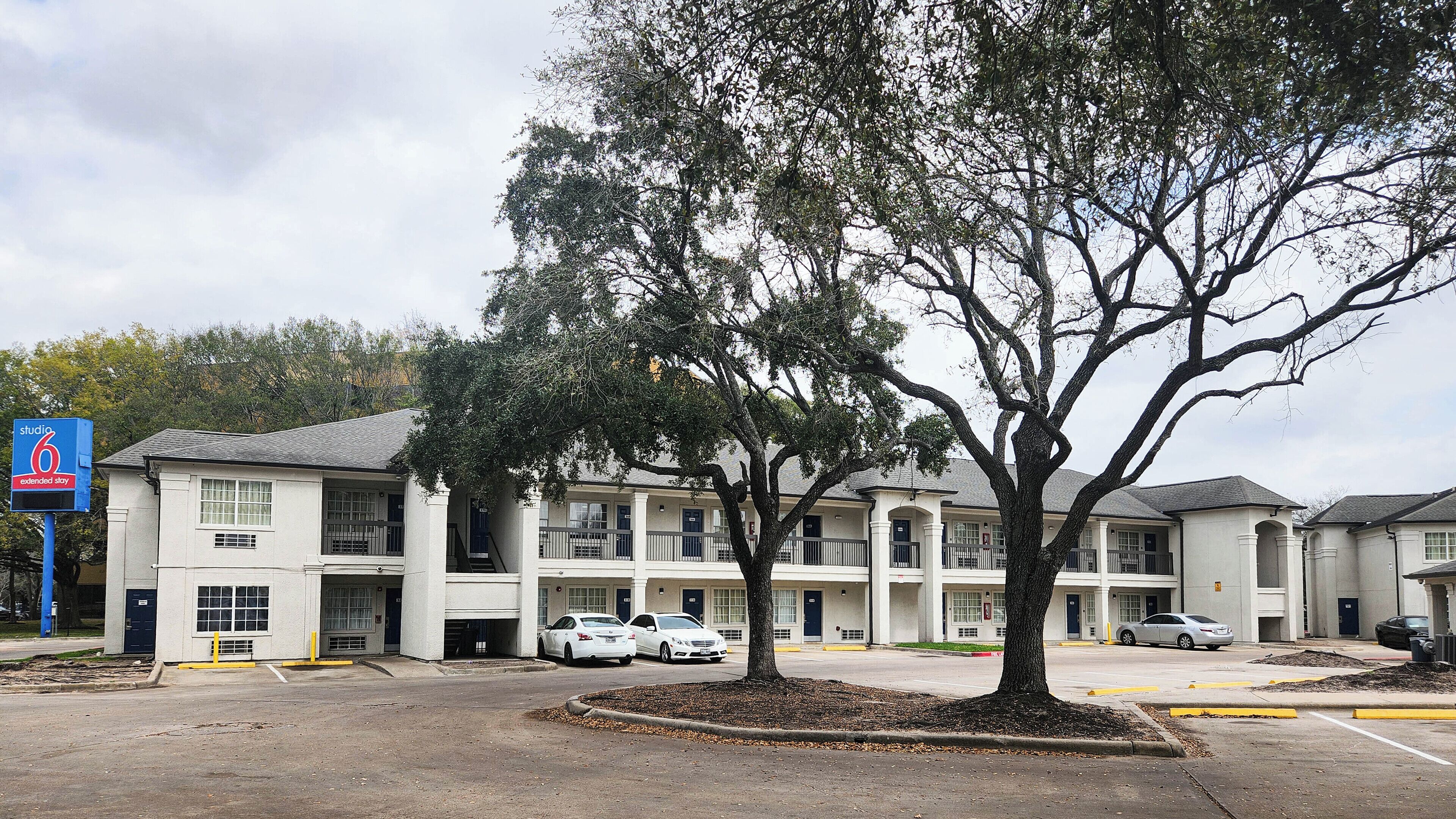 A multi-story hotel with a parking lot, a tree in the foreground, and several cars parked.