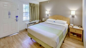 A hotel room with a bed, bedside lamps, a wooden nightstand, a window with curtains, and a door.