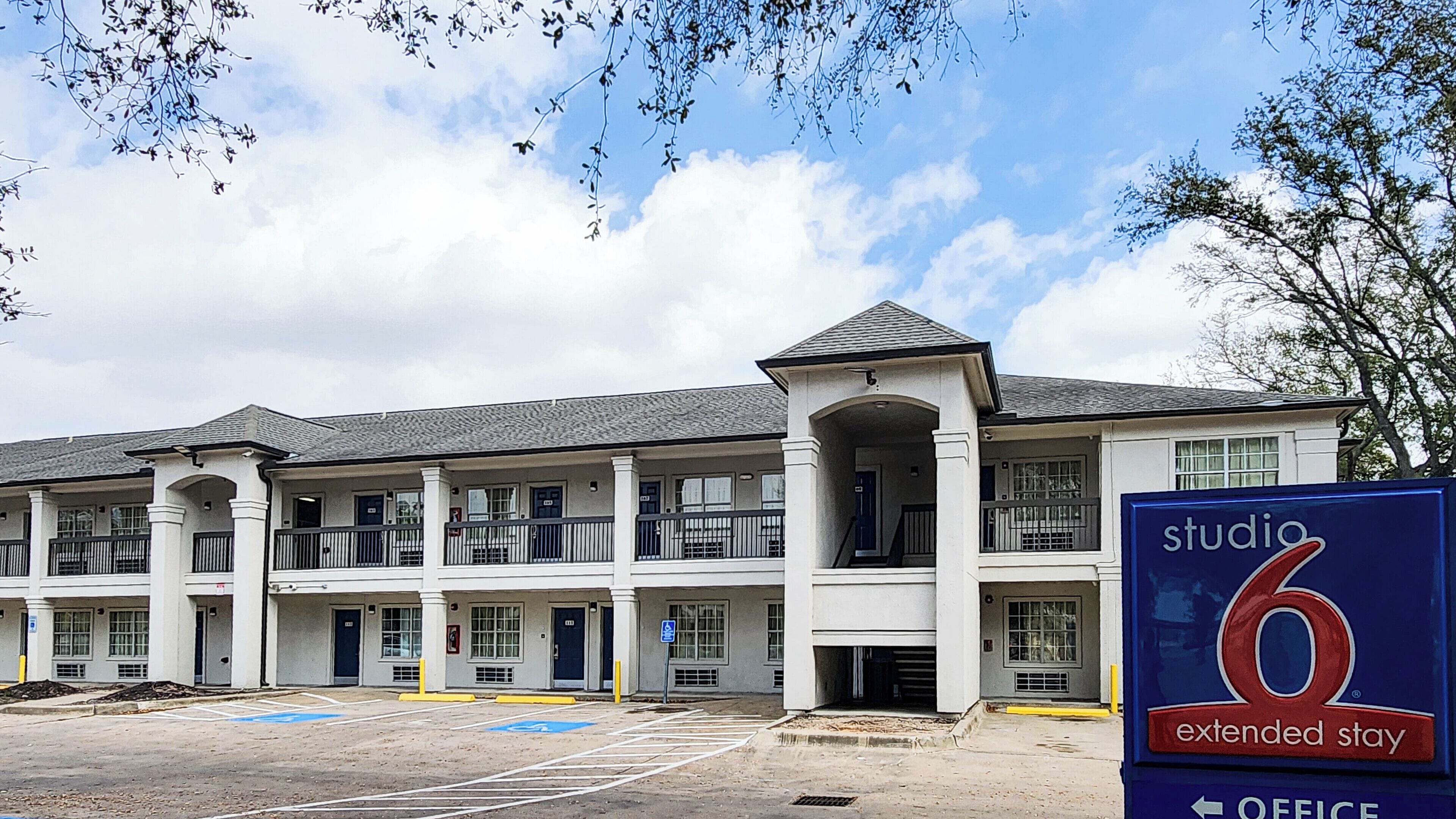 A multi-story hotel with a central courtyard, a sign for 'Studio 6 Extended Stay', and a parking lot with marked spaces.