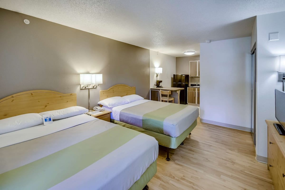 A hotel room with two beds, a desk, a chair, a television, and a bathroom.