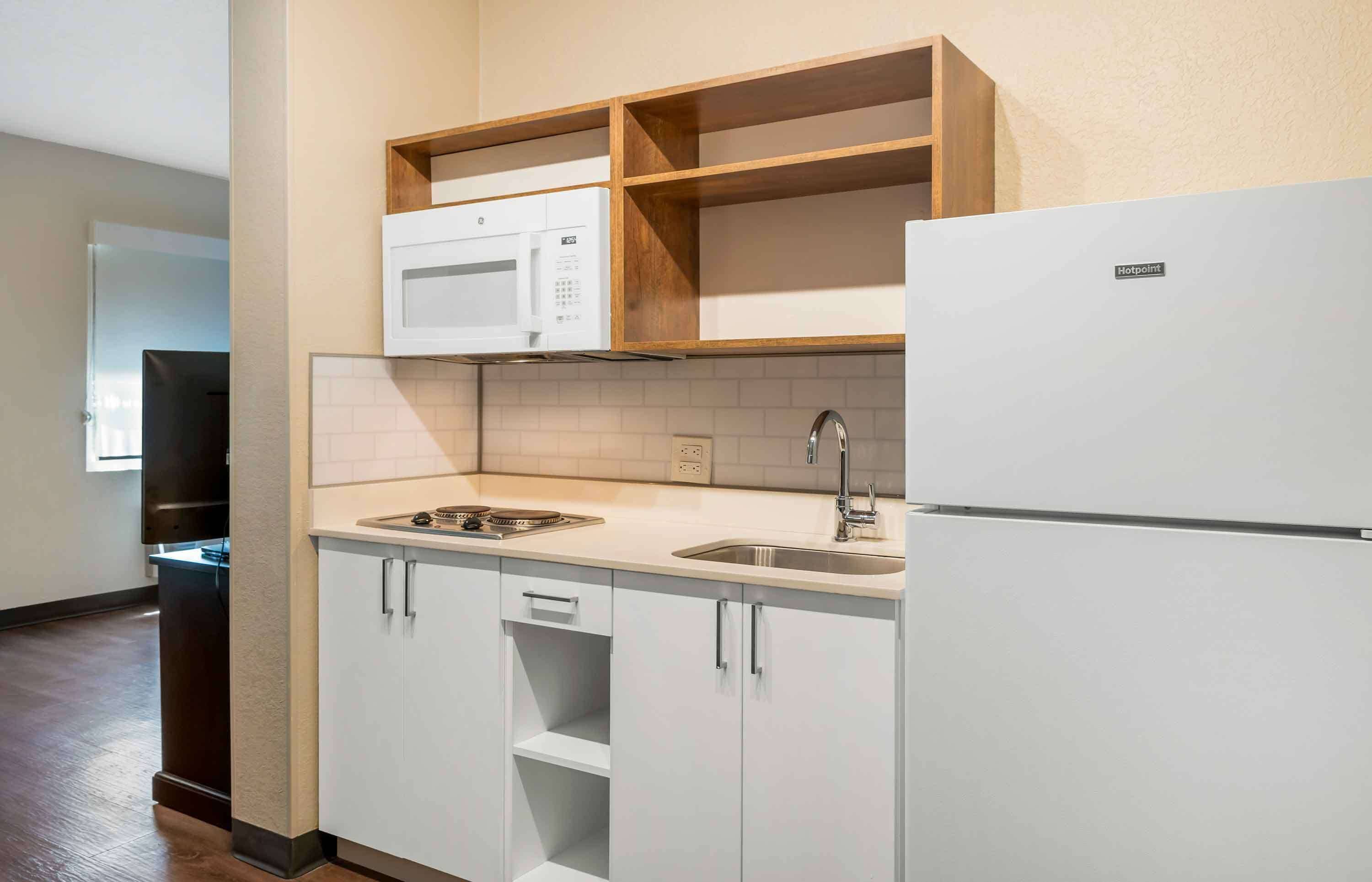 Una cocina compacta con armarios blancos, microondas, fregadero y refrigerador.