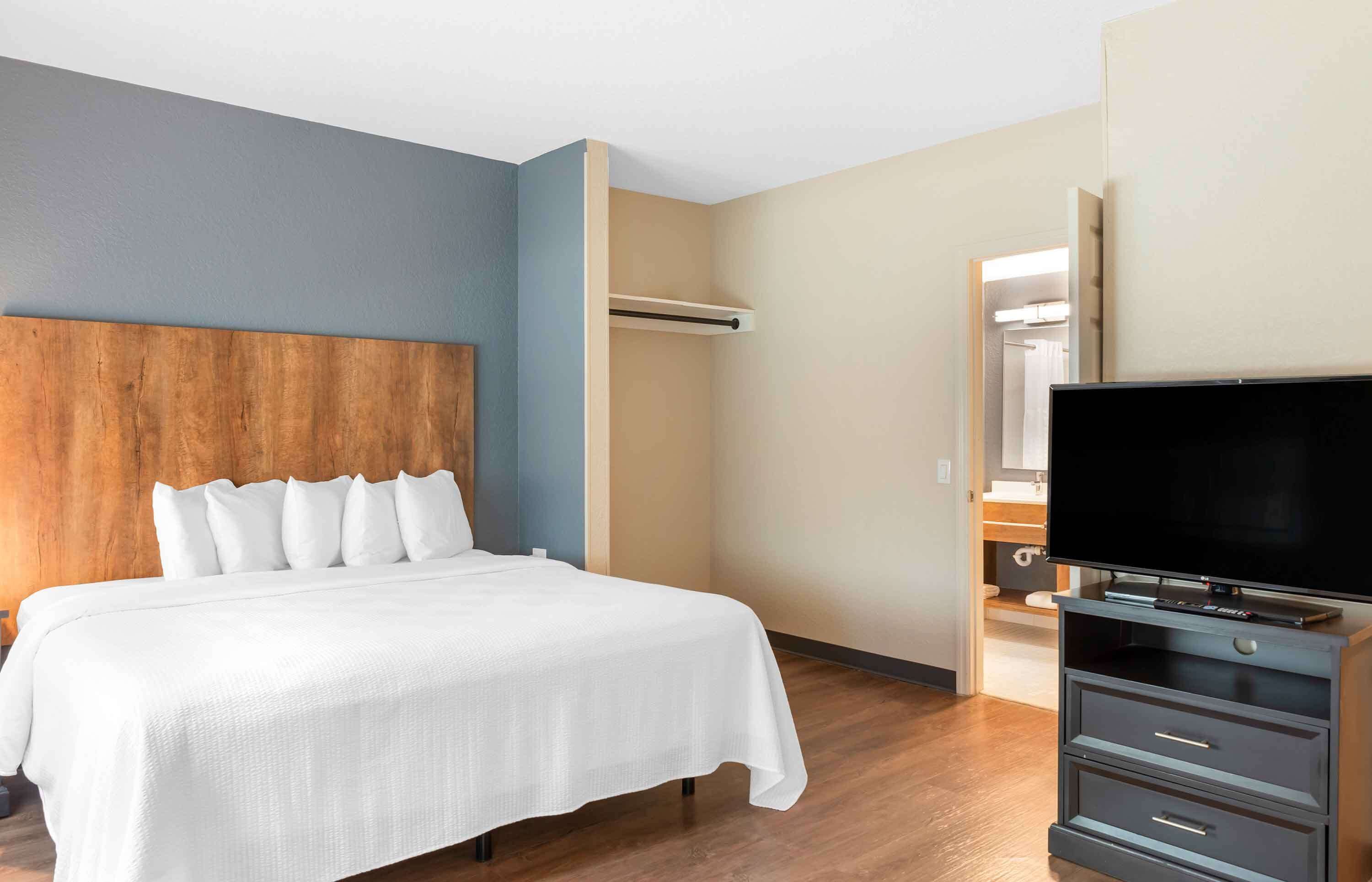 Habitación de hotel con una cama, televisión, armario y baño visible a través de una puerta abierta.