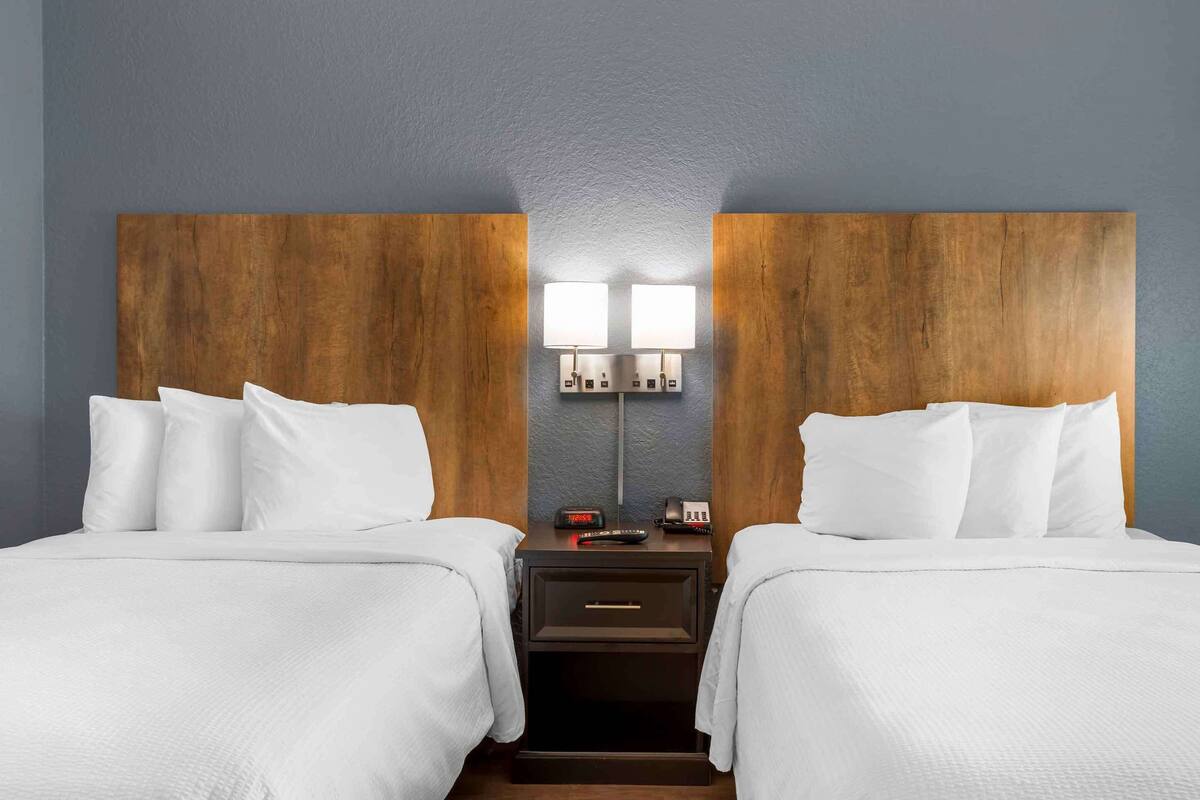 Ein Hotelzimmer mit zwei Betten, einem Holzkopfstück, Nachttischlampen, einem Nachttisch und einem Telefon.