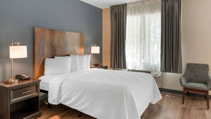 A hotel room with a large bed, two bedside tables with lamps, a chair, and a window with curtains.