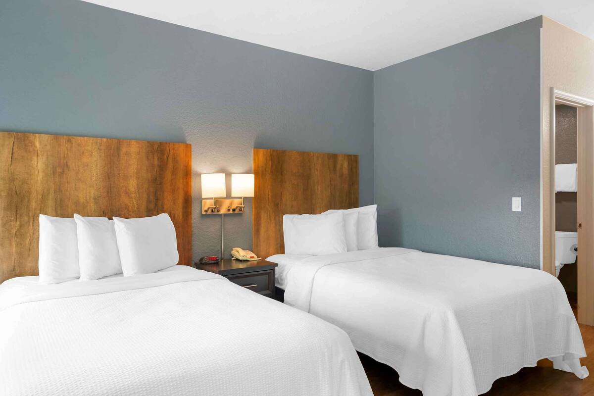 Ein Hotelzimmer mit zwei Betten, einem Nachttisch mit Lampe und einem hölzernen Kopfteil.