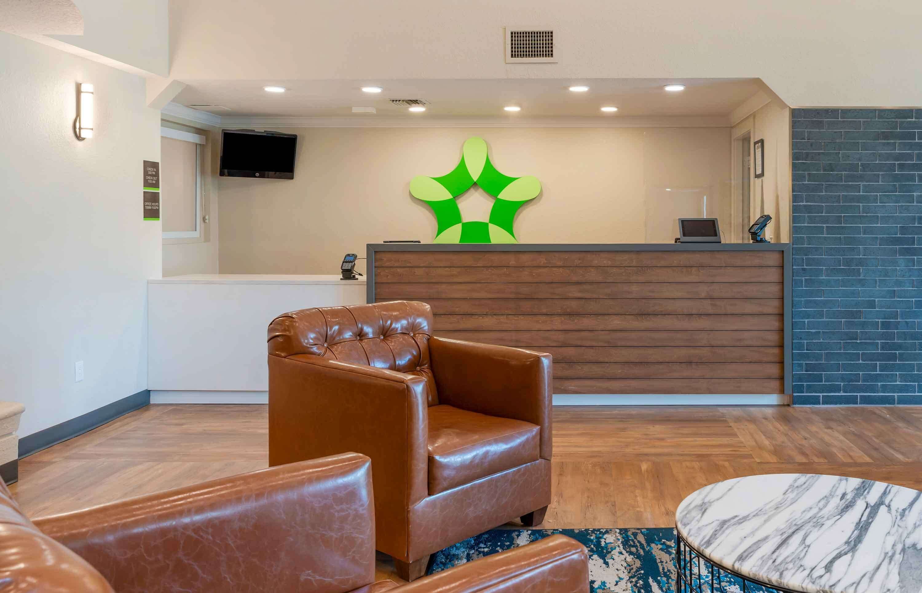 A reception area with a wooden reception desk, a large green wall art piece, and a leather armchair.