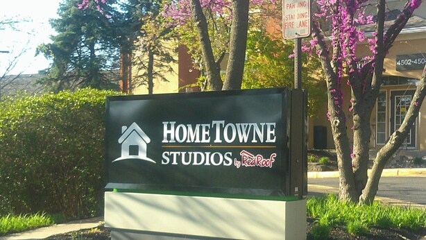 Une enseigne pour Home Towne Studios by Red Roof, avec un logo représentant une maison et du texte.