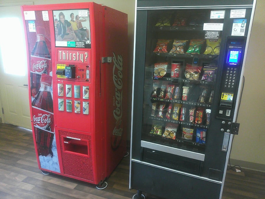 Two vending machines, one red Coca-Cola and one black with various snacks.
