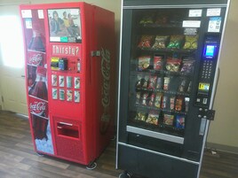Dos máquinas expendedoras, una roja de Coca-Cola y otra negra con diferentes bocadillos.