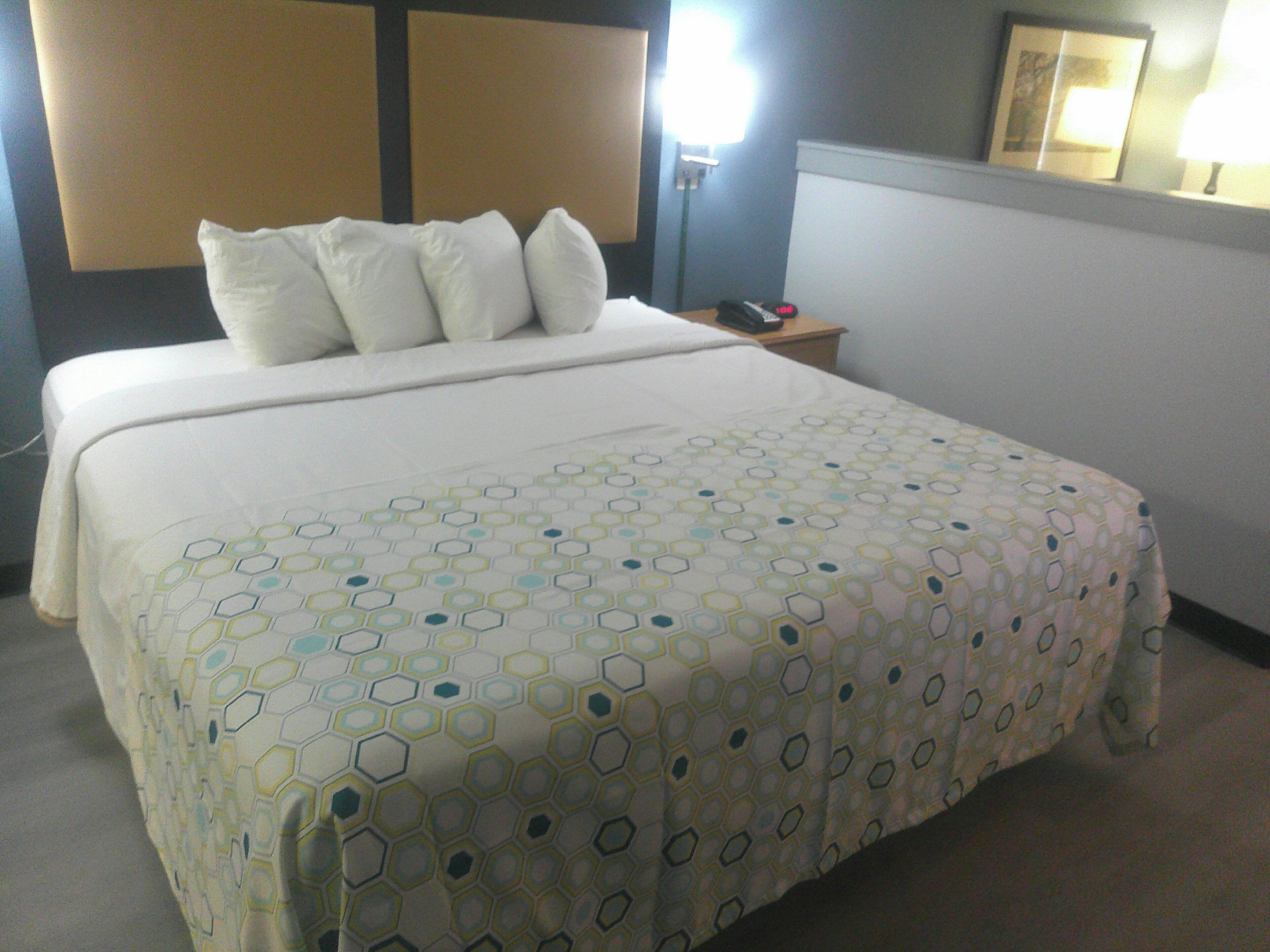 A neatly made bed with a patterned bedspread, a bedside table with a lamp, and a wall-mounted picture frame.