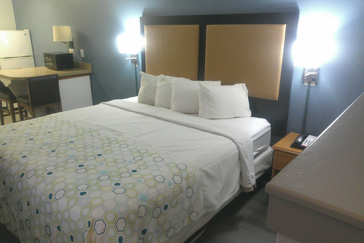 A hotel room with a bed, a desk, a chair, a telephone, and a lamp.