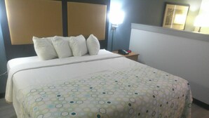 Un lit bien fait, recouvert d’une couvre-lit à motifs, une table de chevet avec une lampe et un cadre photo accroché au mur.