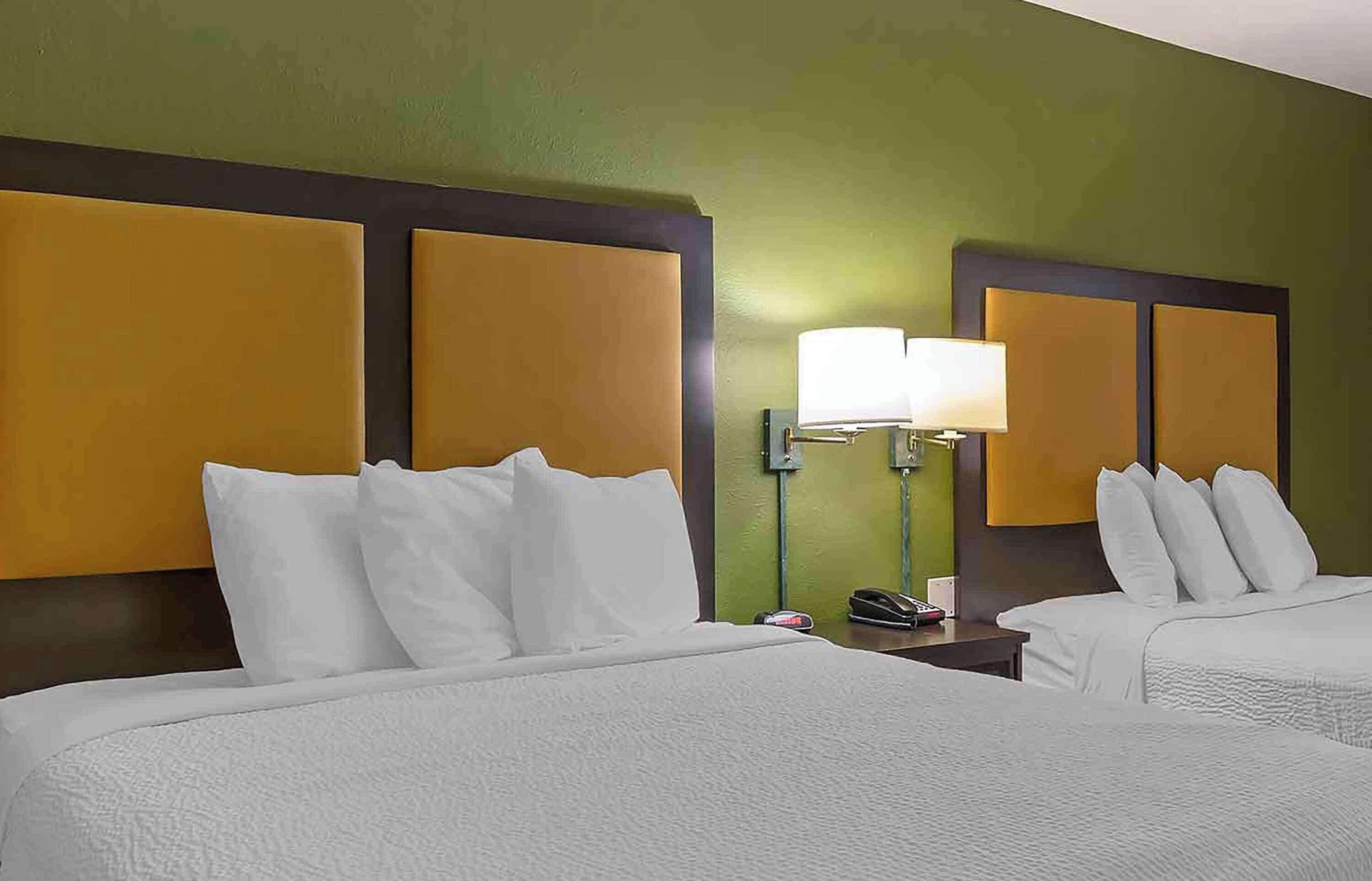 Habitación de hotel con dos camas, una mesita de noche con lámpara y un teléfono.