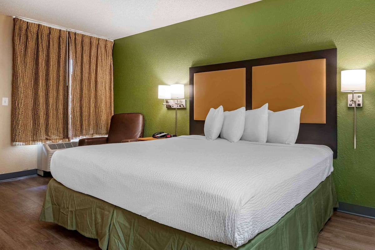 A hotel room with a large bed, a chair, a desk, and a lamp.