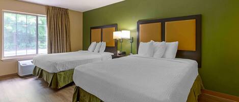 A hotel room with two beds, green walls, and a large window.