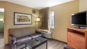 Habitación de hotel con sofá, televisión sobre un mueble de madera, un cuadro en la pared y una ventana con cortinas.