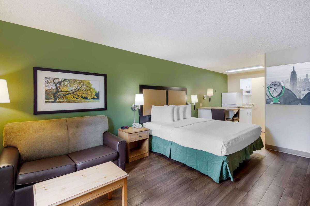A hotel room with a bed, a desk, a chair, a couch, and a small table.