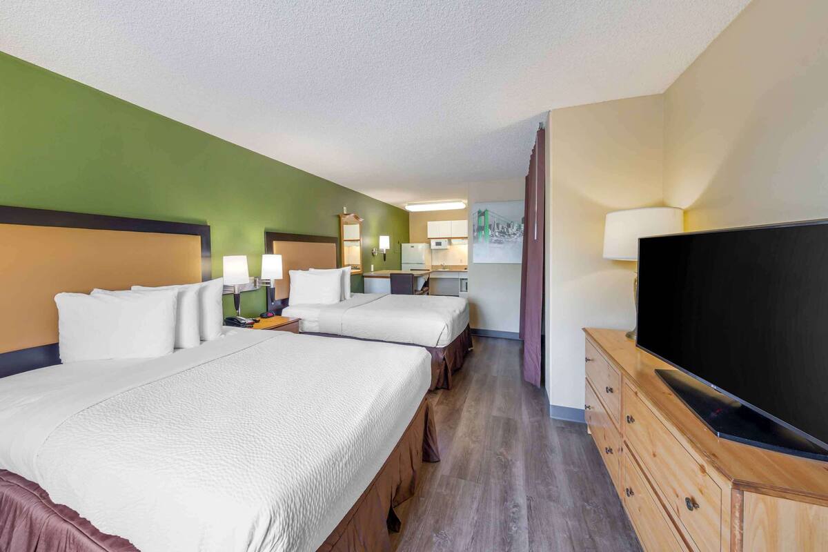 A hotel room with two beds, a TV, a desk with a lamp, and a painting on the wall.