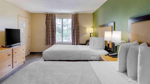 A hotel room with two beds, a television, a desk with a lamp, and a window with curtains.