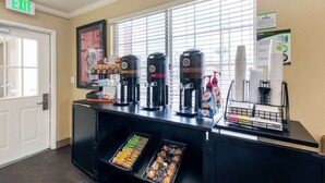 A coffee station with multiple coffee makers, a refrigerator with snacks, and an exit sign.