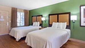 Een hotelkamer met twee bedden, een raam met gordijnen, een groene wand en een houten vloer.