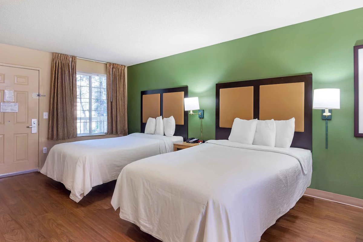 Une chambre d’hôtel avec deux lits, une fenêtre avec des rideaux, un mur vert et un plancher en bois.